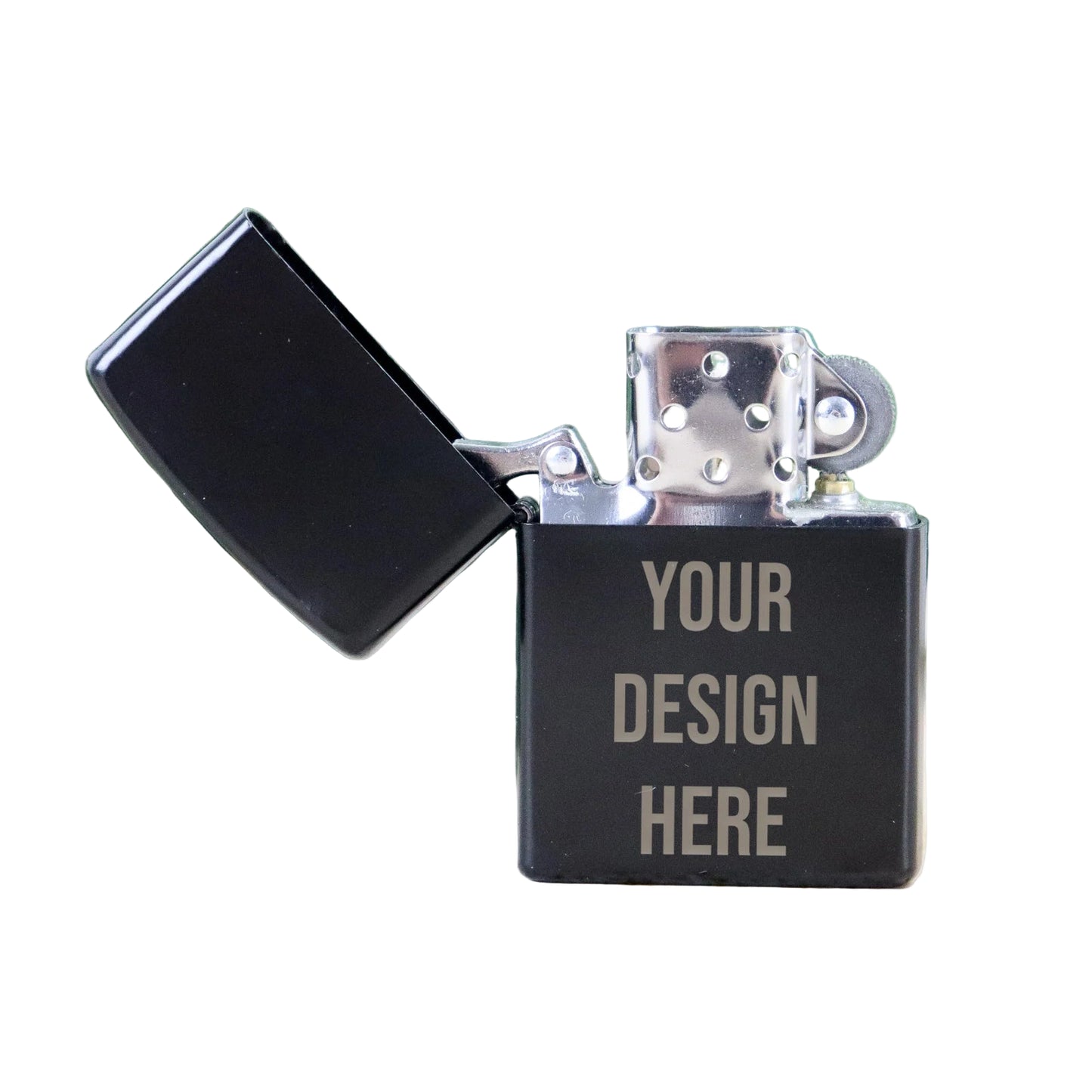 Black Zippo-style lighter with 'Your Design Here' text on a light wood surface with green leaves in the background.