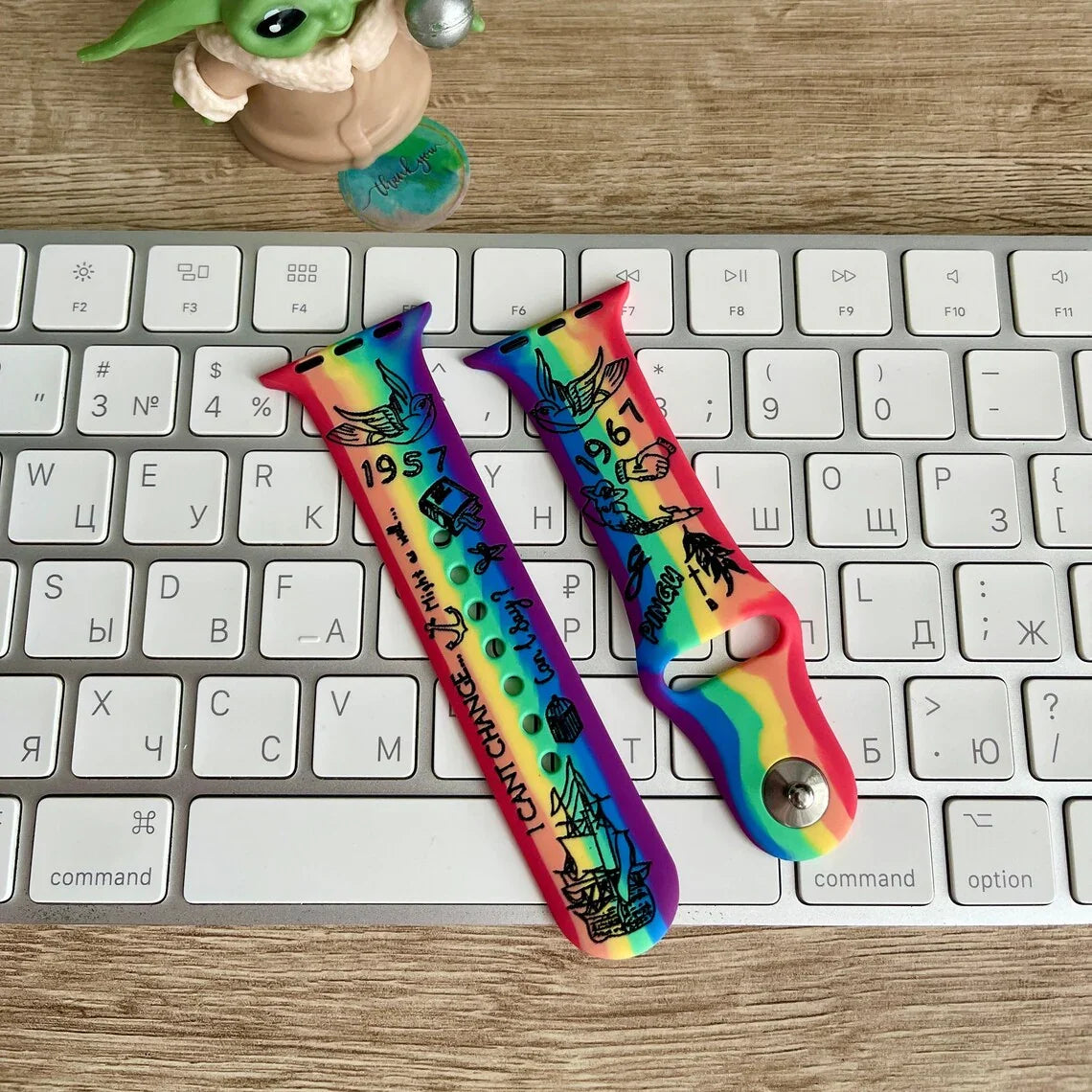 Rainbow Pride Apple Watch straps with black graphic designs on a keyboard