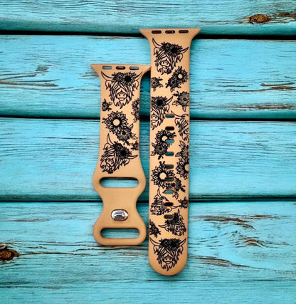 Beige Apple Watch straps with black floral and cow designs on teal wooden background