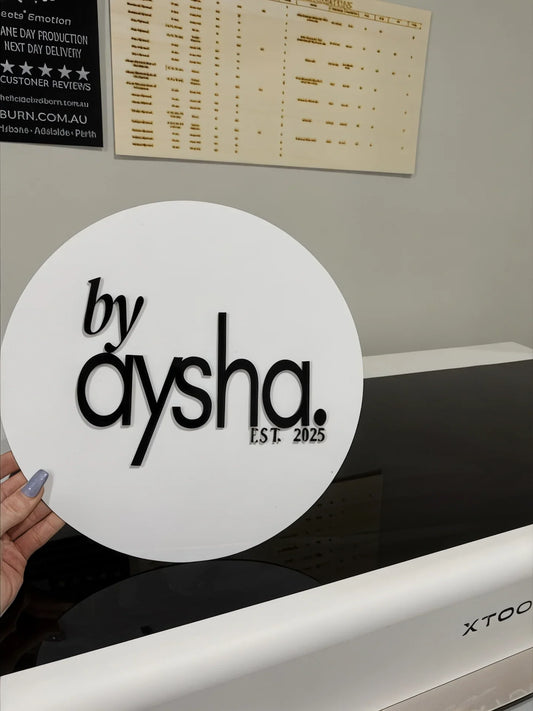 Hand holding custom round acrylic sign by aysha EST. 2025 in workshop setting
