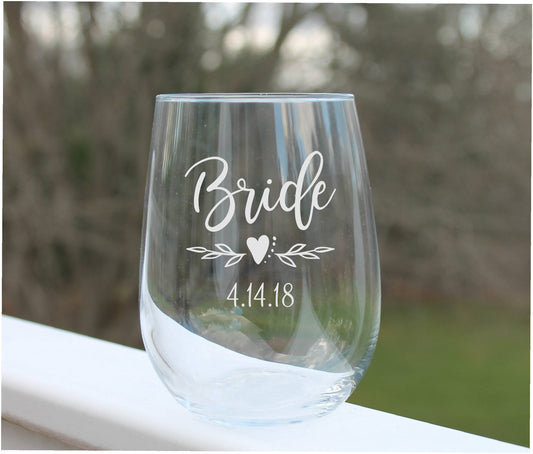 Clear wine glass with 'Bride' and '4.14.18' engraving on a blurred natural background