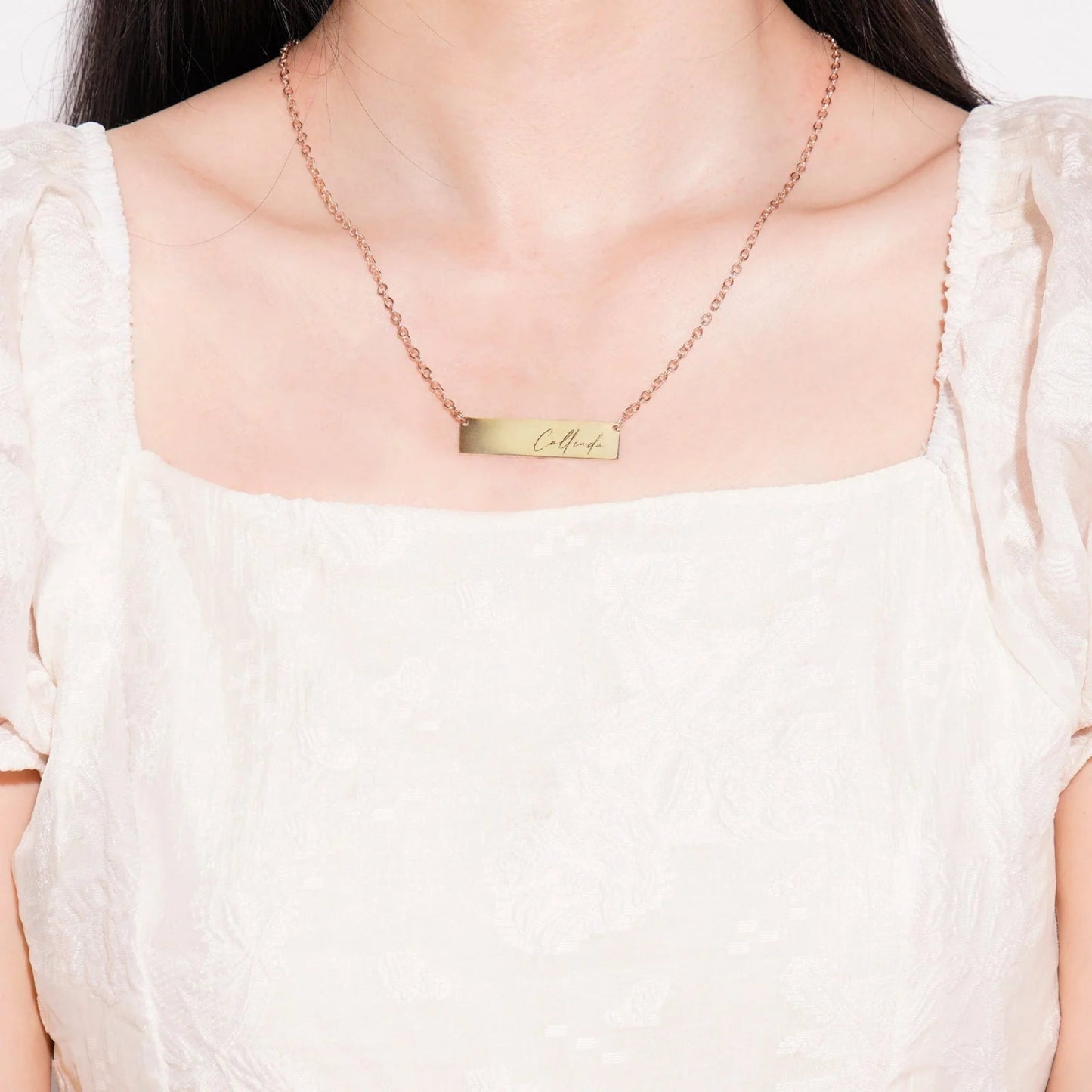 Gold necklace with a nameplate worn by a person on a white background