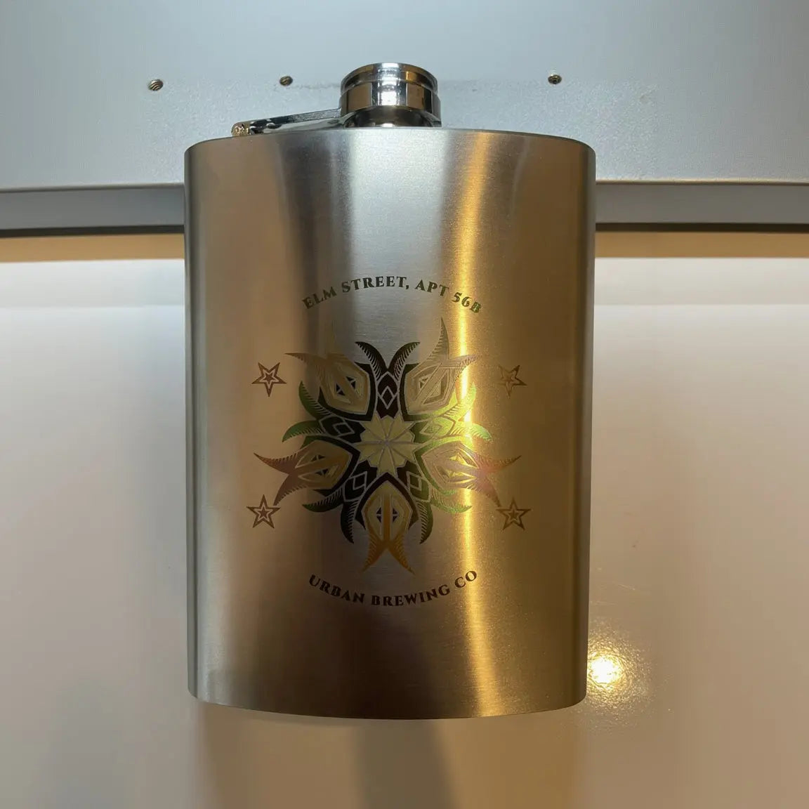 Metallic flask with 'Urban Brewing Co' logo on a reflective surface