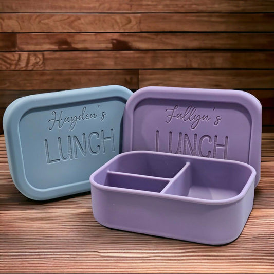 Two lunch containers with personalised names on a wooden surface